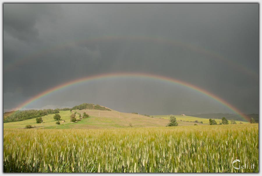 Arcobaleno delicato e fantastico con presenza di arco secondario su colline inondate dalla pioggia 