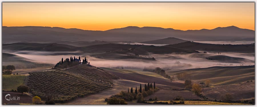 Vista mozzafiato dalla collina, con nebbia su pianure e colline, podere protettivo, luccichio dorato nel terreno, visione incantevole e pacifica 