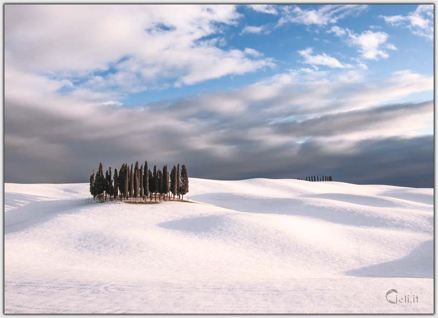 Paesaggio innevato con cipressi e squarcio azzurro nel cielo
